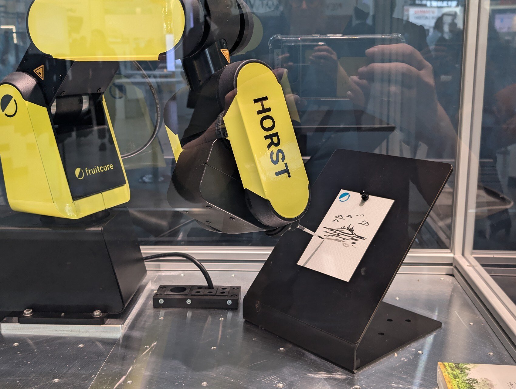 A yellow Horst600 robot arm with an attached paintbrush drawing on a whie card